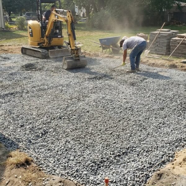 Workers leveling and spreading gravel with equipment and wheelbarrows during outdoor construction